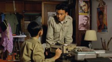 two young Taiwanese boys in military uniforms talk to each other over a tape recorder with Elvis posters in the background